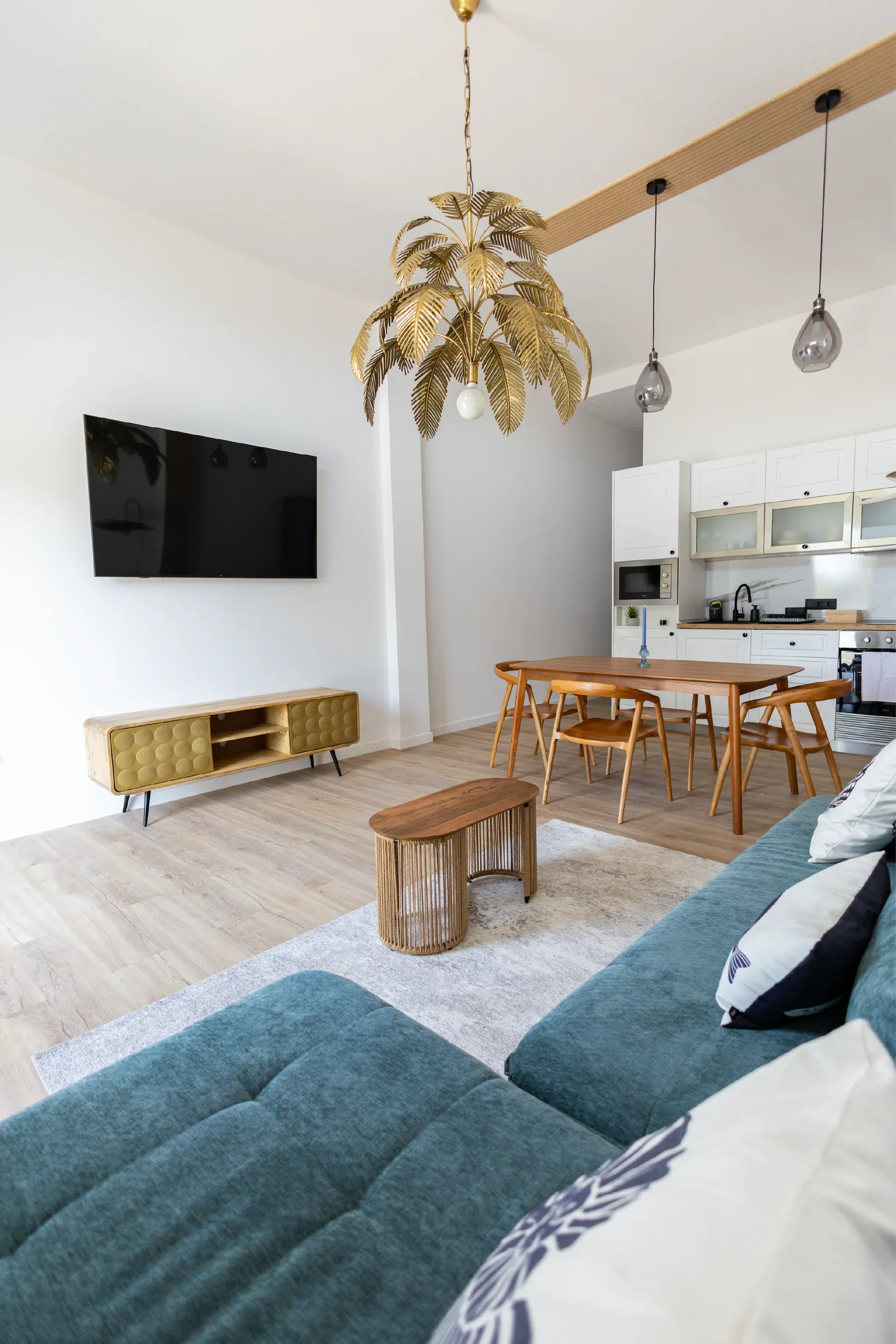 Salón con sofá teal, cocina y candelabro dorado en una de las viviendas vacacionales