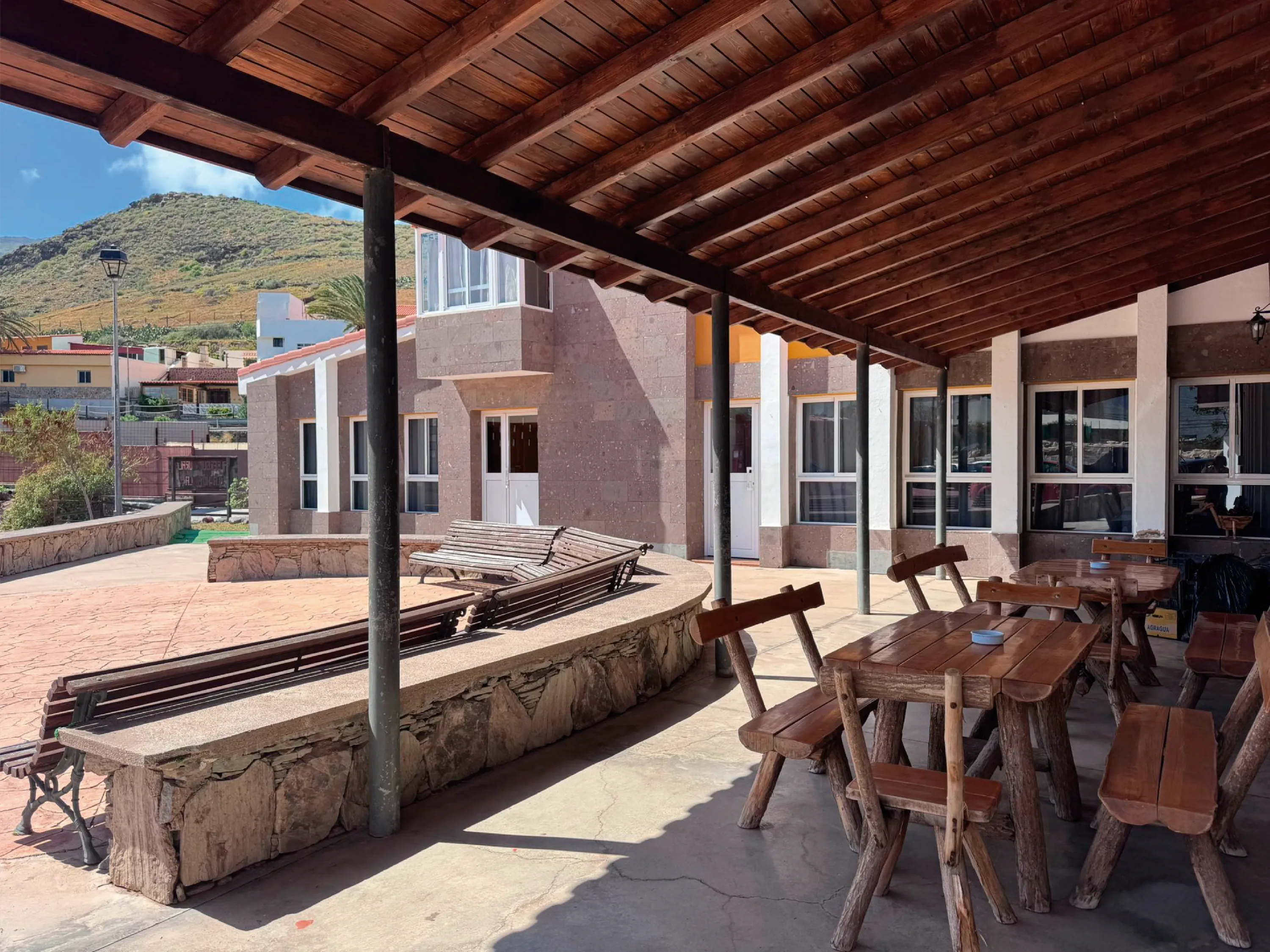 Terraza exterior del Albergue La Hoyilla de Lemusa Stays, con mesas rústicas de madera y montañas al fondo